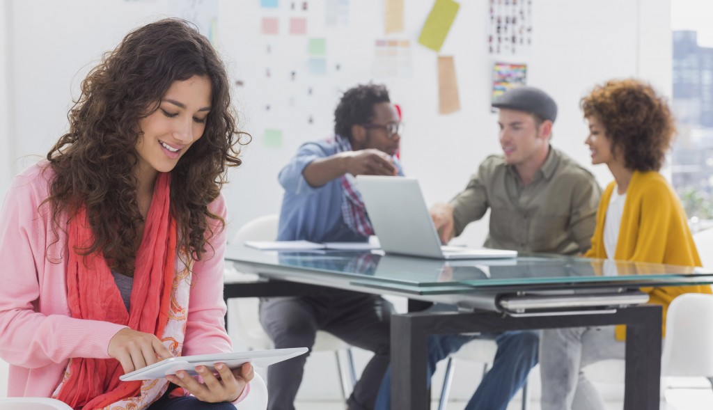 Smiling designer using digital tablet with team at work behind her